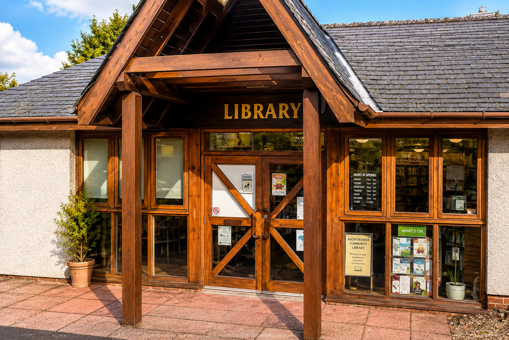 Exterior of Auchterarder Library with its timber entrance, slate roof, and large windows displaying library information and notices.